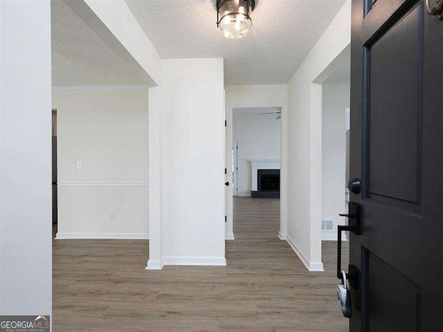 entryway with a textured ceiling, a ceiling fan, baseboards, and wood finished floors