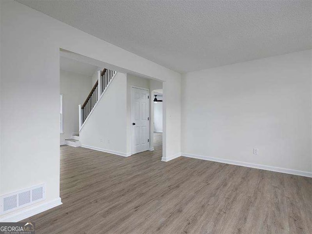 empty room with visible vents, baseboards, a textured ceiling, and wood finished floors