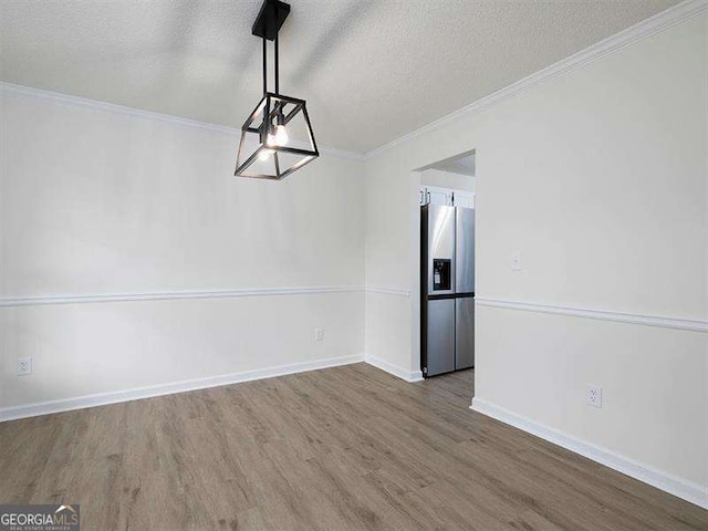 unfurnished dining area with crown molding, wood finished floors, baseboards, and a textured ceiling