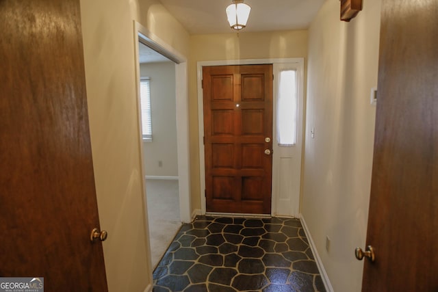 foyer entrance with baseboards and dark carpet