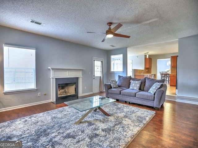 living area featuring a ceiling fan, dark wood-style floors, visible vents, baseboards, and a fireplace with flush hearth