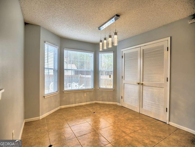 unfurnished dining area with tile patterned flooring, baseboards, and a textured ceiling