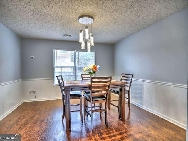 dining area with visible vents, a textured ceiling, wood finished floors, and a chandelier