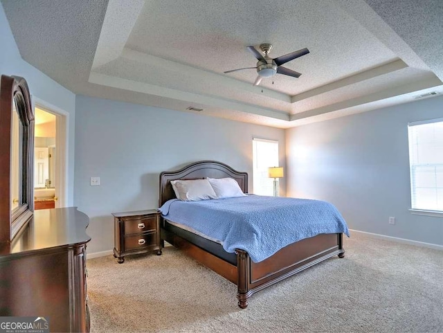 bedroom with a tray ceiling, light colored carpet, visible vents, and a textured ceiling