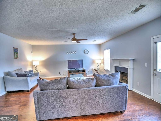 living room with dark wood finished floors, visible vents, a fireplace, and ceiling fan