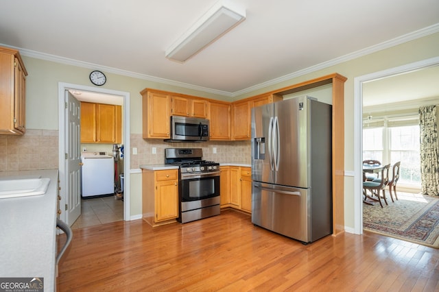 kitchen featuring light wood-style flooring, appliances with stainless steel finishes, crown molding, light countertops, and washer / dryer