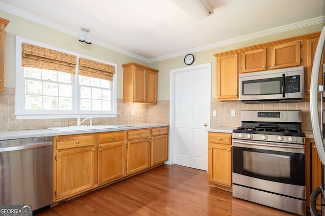 kitchen with crown molding, light countertops, wood finished floors, stainless steel appliances, and a sink