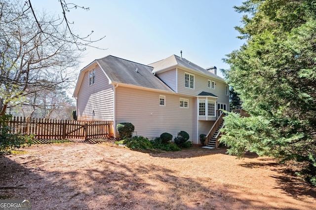 back of property with stairway, fence, and a shingled roof