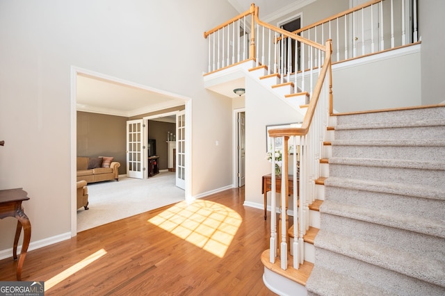 stairs featuring wood finished floors, baseboards, ornamental molding, french doors, and a towering ceiling