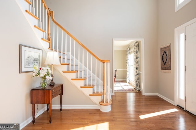 entryway with stairs, a high ceiling, baseboards, and wood finished floors