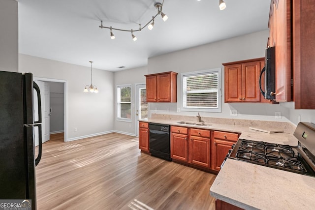 kitchen with light wood finished floors, light countertops, a notable chandelier, black appliances, and a sink