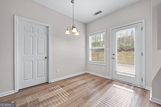 unfurnished dining area with an inviting chandelier, wood finished floors, visible vents, and baseboards