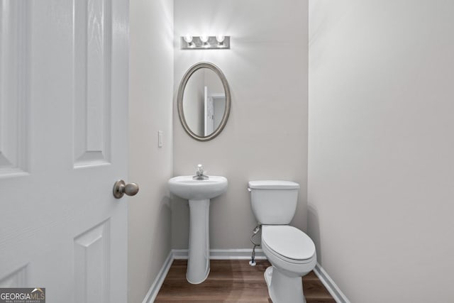 half bathroom with baseboards, toilet, and wood finished floors