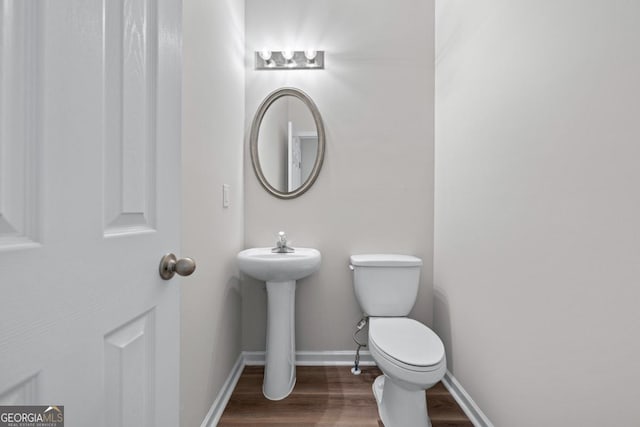 half bathroom with toilet, baseboards, and wood finished floors