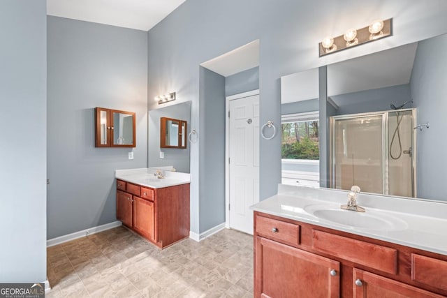 bathroom featuring a shower stall, two vanities, baseboards, and a sink