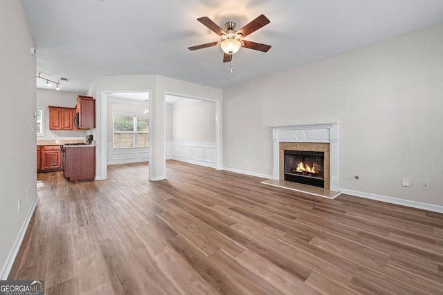 unfurnished living room with a high end fireplace, baseboards, rail lighting, wood finished floors, and a ceiling fan