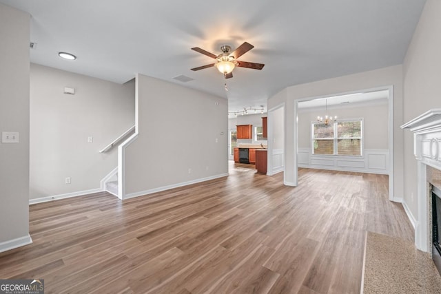 unfurnished living room with stairway, ceiling fan with notable chandelier, a fireplace, and light wood-type flooring