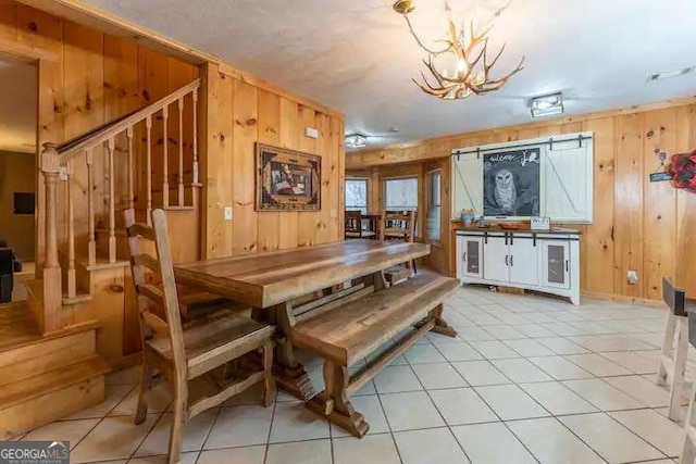 dining space featuring light tile patterned floors, a chandelier, stairs, and wood walls