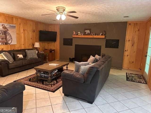 living room featuring light tile patterned flooring, a textured ceiling, wood walls, and a ceiling fan