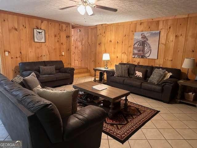 living area with light tile patterned floors, a textured ceiling, ceiling fan, and wooden walls