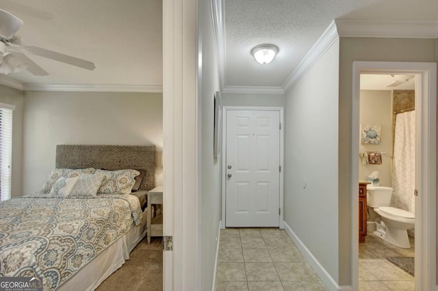 bedroom featuring crown molding, baseboards, light tile patterned floors, ensuite bath, and a textured ceiling