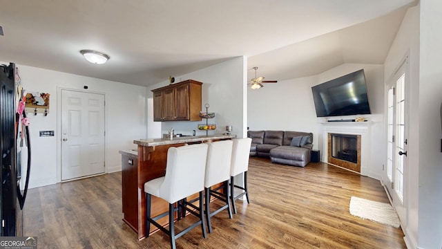 kitchen featuring a kitchen breakfast bar, wood finished floors, a peninsula, a fireplace, and vaulted ceiling