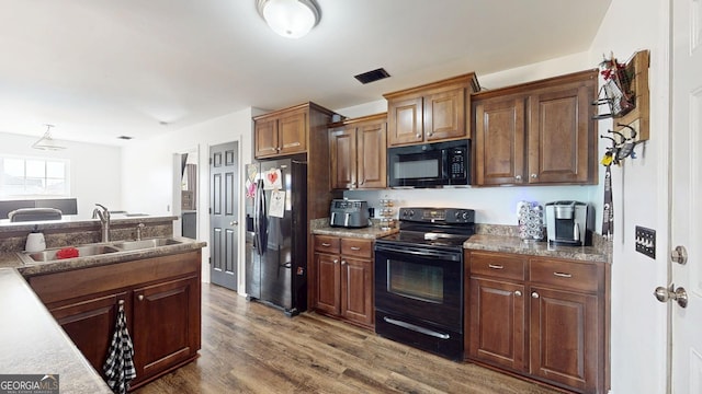 kitchen with visible vents, black appliances, dark wood-type flooring, and a sink