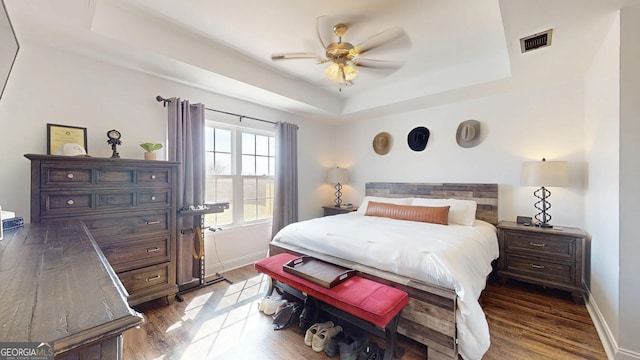 bedroom with visible vents, baseboards, a tray ceiling, and wood finished floors