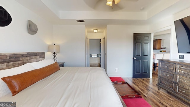 bedroom featuring visible vents, baseboards, wood finished floors, a raised ceiling, and a ceiling fan