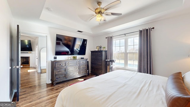 bedroom with a ceiling fan, a tray ceiling, and wood finished floors