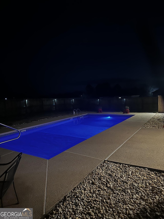 pool at night featuring a fenced in pool and a patio