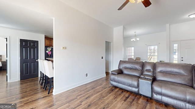 living area with dark wood-style floors, ceiling fan with notable chandelier, and baseboards