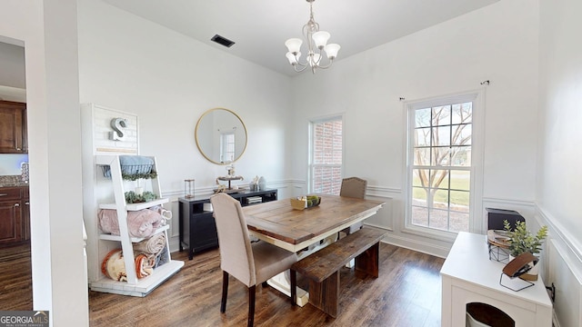 dining room with wood finished floors, visible vents, wainscoting, a decorative wall, and a chandelier