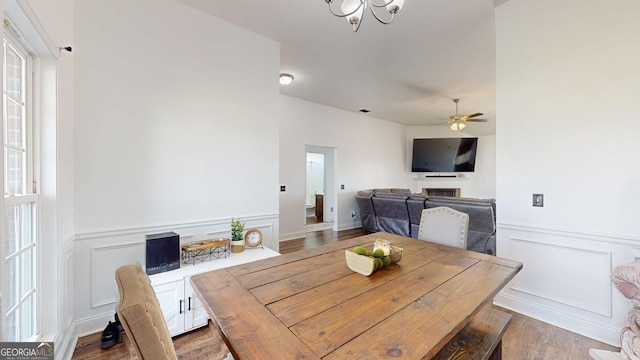 dining room featuring a wainscoted wall, ceiling fan with notable chandelier, a fireplace, wood finished floors, and a decorative wall