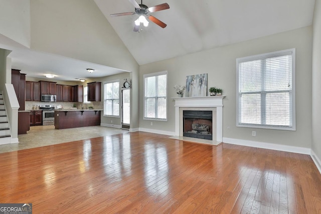 unfurnished living room with high vaulted ceiling, a ceiling fan, light wood-style floors, a fireplace, and baseboards