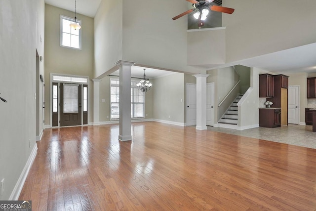 entryway featuring light wood finished floors, ceiling fan with notable chandelier, baseboards, and ornate columns