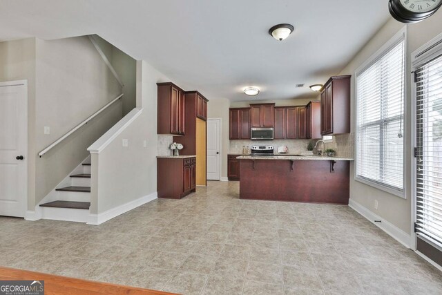 kitchen with backsplash, appliances with stainless steel finishes, a breakfast bar area, a peninsula, and baseboards