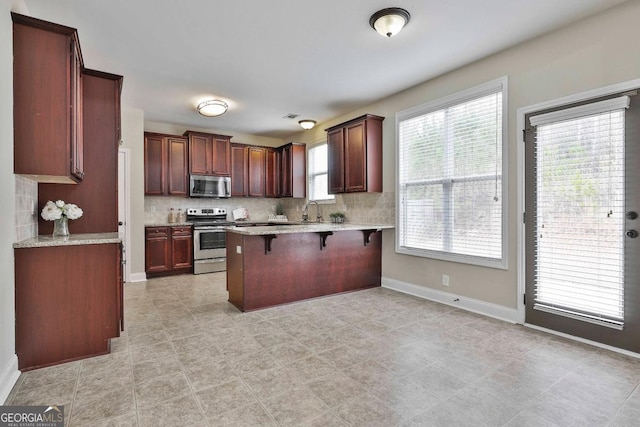 kitchen with stainless steel appliances, a kitchen bar, backsplash, and a peninsula