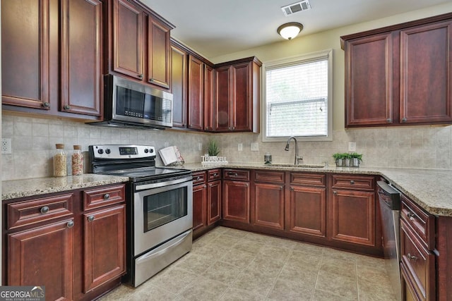 kitchen with visible vents, a sink, stainless steel appliances, reddish brown cabinets, and decorative backsplash