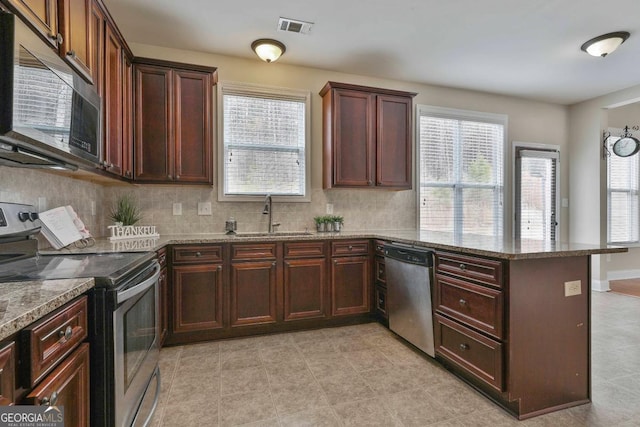 kitchen with visible vents, a peninsula, stone countertops, a sink, and appliances with stainless steel finishes