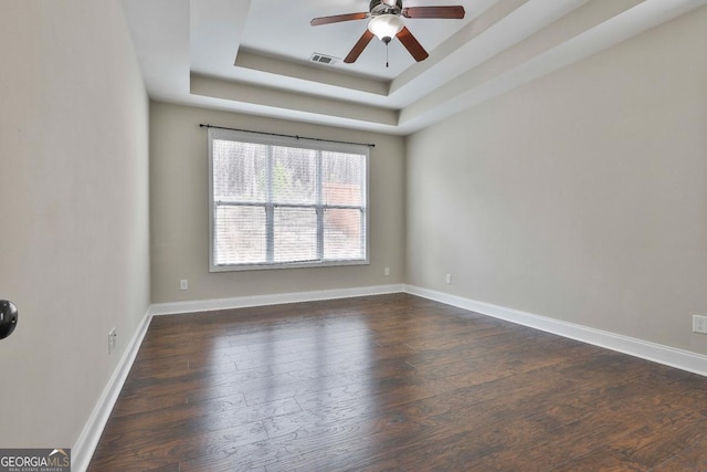 empty room featuring visible vents, a ceiling fan, dark wood-style floors, baseboards, and a raised ceiling