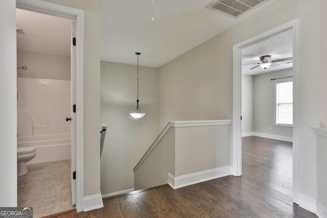 hall featuring an upstairs landing, visible vents, baseboards, and wood finished floors