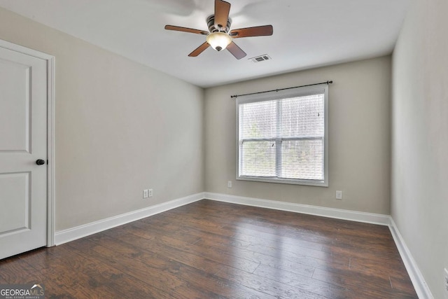 empty room with dark wood-style floors, visible vents, a ceiling fan, and baseboards