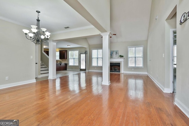 unfurnished living room featuring visible vents, decorative columns, a fireplace, light wood-style floors, and a notable chandelier