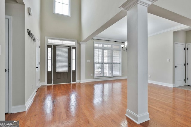 entrance foyer with baseboards, wood-type flooring, a chandelier, and ornate columns