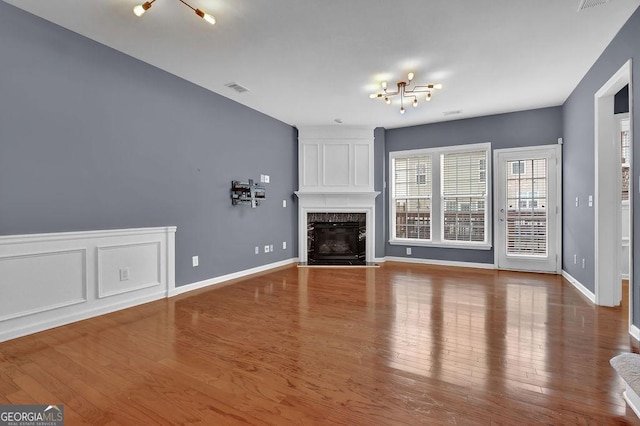 unfurnished living room with a premium fireplace, wood finished floors, visible vents, and a chandelier