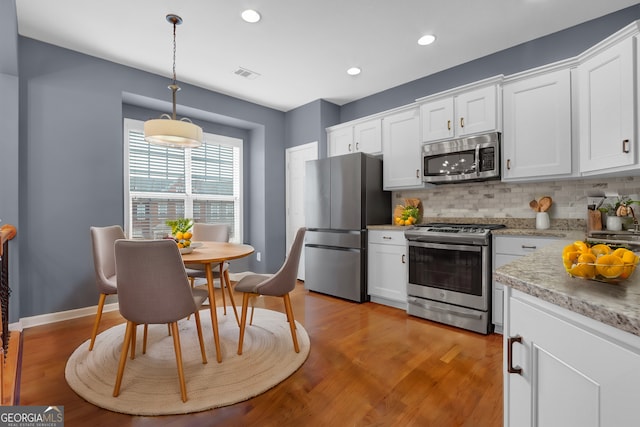 kitchen featuring visible vents, light wood-style flooring, backsplash, appliances with stainless steel finishes, and white cabinets