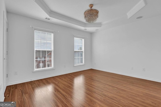 empty room with wood finished floors, visible vents, baseboards, a tray ceiling, and crown molding