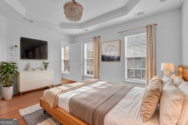 bedroom featuring visible vents, a raised ceiling, light wood-style flooring, and crown molding