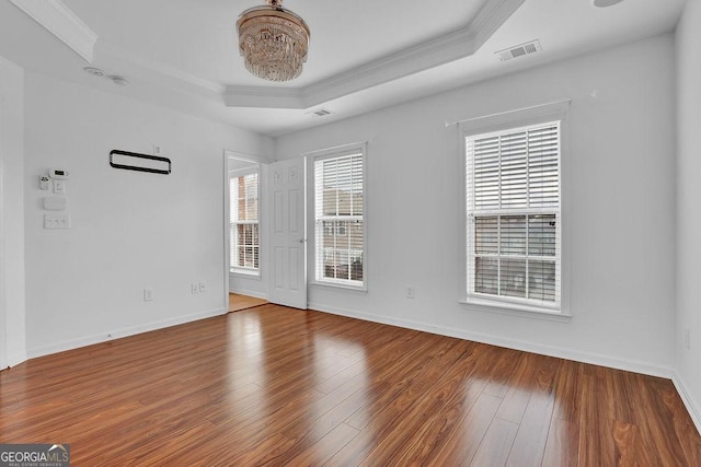 spare room with visible vents, baseboards, ornamental molding, wood finished floors, and a raised ceiling